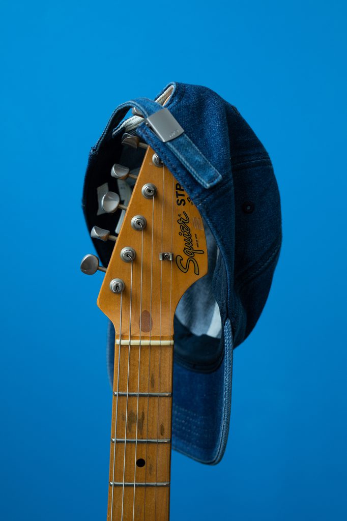 jeanscap-hängt-über-Gitarrenhals-vor-blauer-Wand