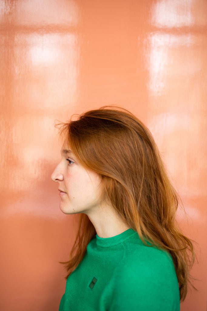Cellistin-mit-roten-Haaren-mit-grünem-Pullover-vor-spiegelnder-Wand